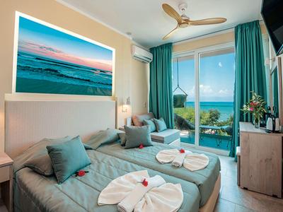 Modern hotel room with two single beds, balcony, and sea view at sunset.