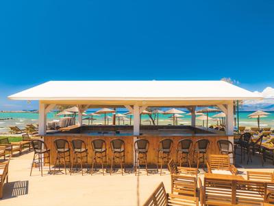 Offene Strandbar mit Stühlen und Tischen vor blauem Himmel und Meer