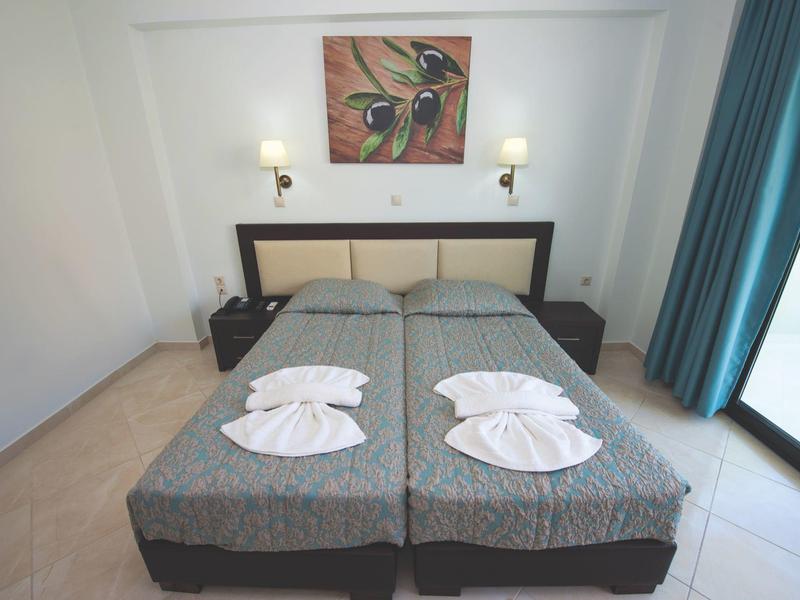 Hotel room with two single beds, nightstands, wall lamps, and bright curtains by the window.