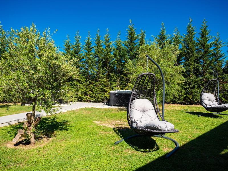 Green garden with shaded hanging chairs and trees under a clear blue sky.