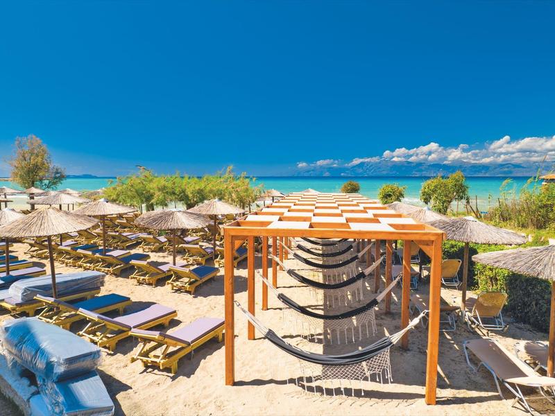 Terrazza con amache e ombrelloni davanti al mare sotto un cielo azzurro.