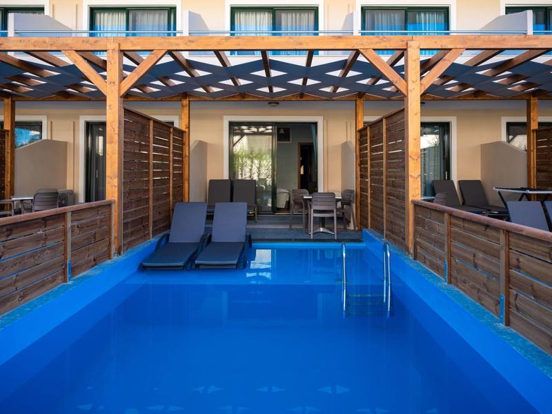 Piscina blu con lettini davanti a un edificio alberghiero moderno.