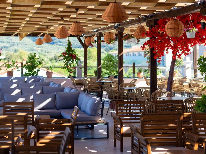 Terrazza ombreggiata con tavoli di legno, divani blu e vista su lago e giardino.