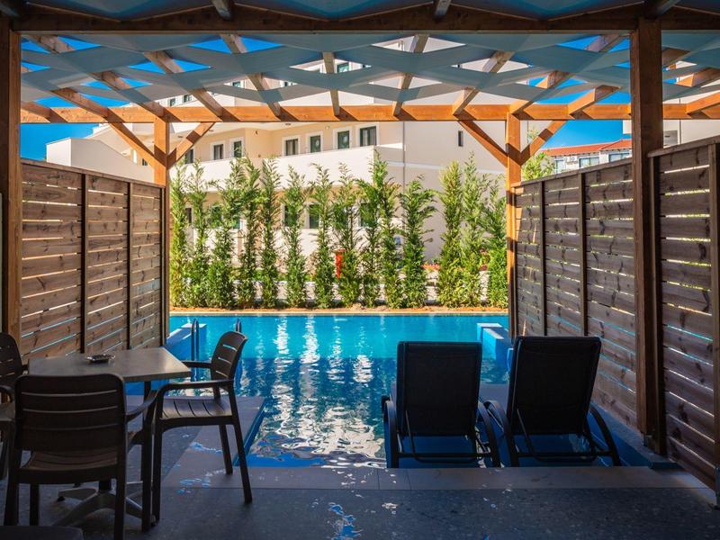 Piscina esterna con lettini sotto una pergola in legno, tavolo e sedie.