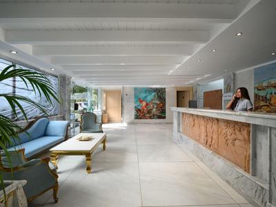 Jasna lobby hotelowa z miejscem do siedzenia, rośliną i recepcją z pracownikiem.