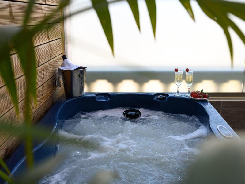 Una vasca idromassaggio esterna con acqua frizzante, circondata da piante e un tavolo con bevande.