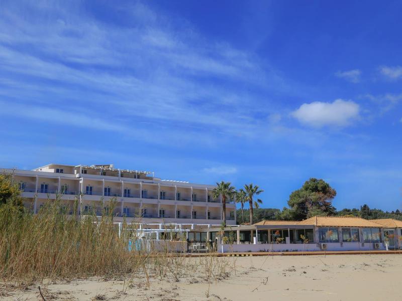 Una struttura alberghiera con terrazze balconate accanto a una spiaggia sotto un cielo azzurro.