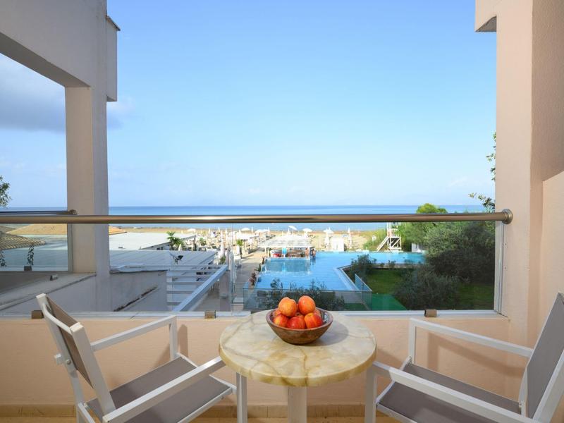 Balcone con due sedie e tavolo con frutta e vista sul mare sotto un cielo limpido.
