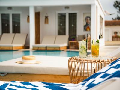 Ein Poolbereich mit Liegestühlen, kissen mit blau-weißem Streifen, und zwei Getränken auf einem Korbtisch.