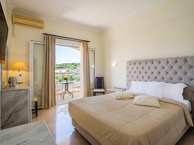 Helles Hotelzimmer mit Doppelbett und Zugang zu einem Balkon mit Aussicht auf grüne Hügel.