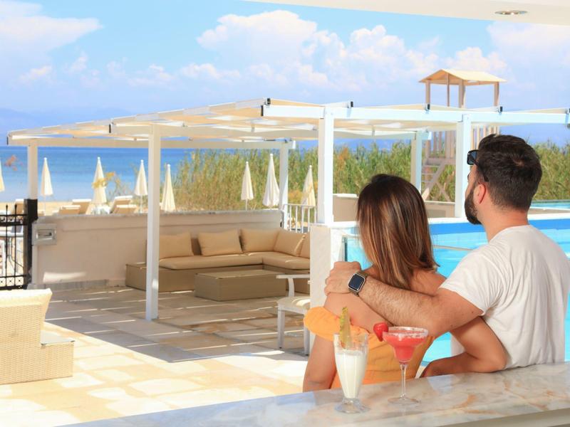 Paar sitzt entspannt auf Terrasse mit Cocktails und Blick auf blauen Himmel und Meer.