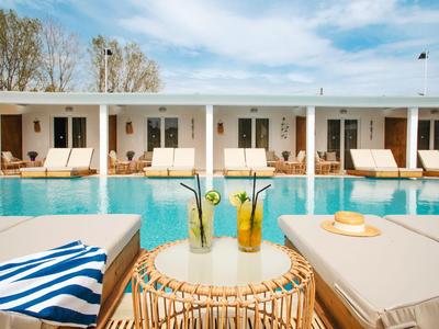 Poolbereich mit Liegestühlen, Getränken und Bungalows im Hintergrund an einem sonnigen Tag.