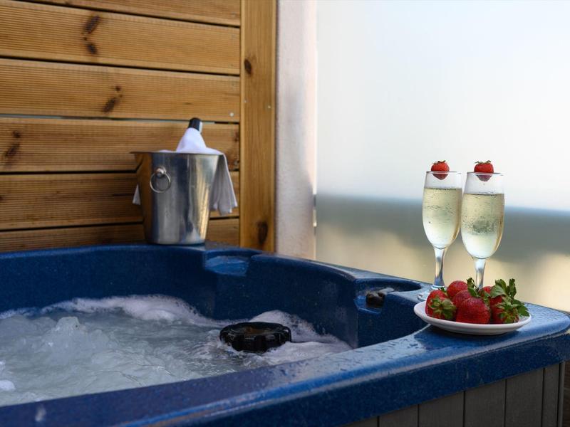 Blauer Whirlpool mit sprudelndem Wasser, daneben Champagnerflasche im Eiskübel und zwei Gläser mit Erdbeeren.