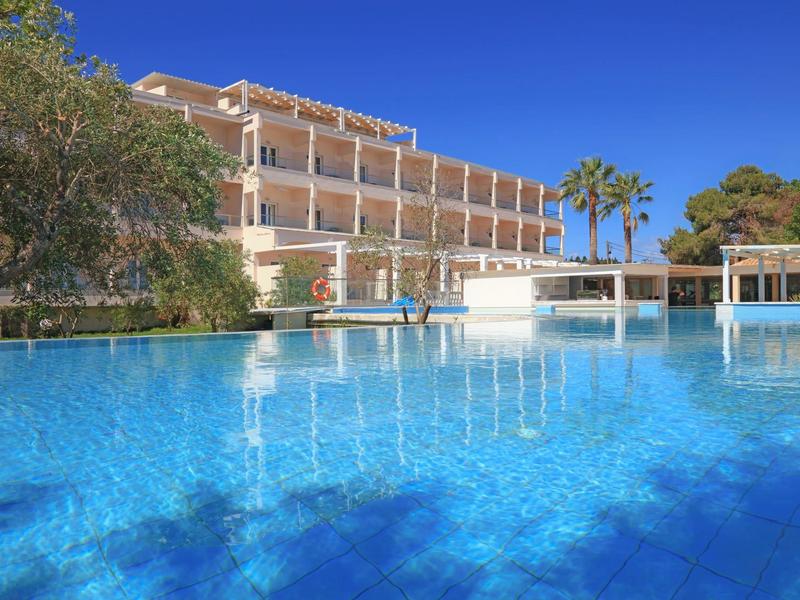 Modernes Hotel mit großem blauen Pool, Palmen und klarem Himmel im Hintergrund.