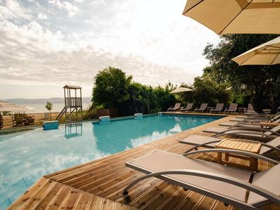 Ruhebereich mit Holzliegen und Pool mit Ausblick auf Strand und Meer bei Sonnenuntergang.