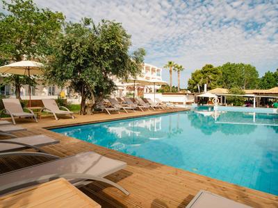 Poolbereich eines Hotels mit Liegestühlen, Sonnenschirmen und Bäumen bei bewölktem Himmel