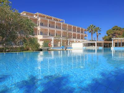 Modernes Hotel mit großem blauen Pool, Palmen und klarem Himmel im Hintergrund.