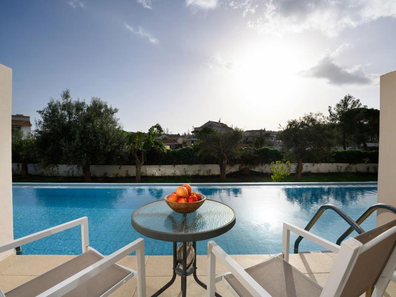 Balcony mit Tisch, Stühlen und Ausblick auf einen Pool und Bäume bei Sonnenschein.