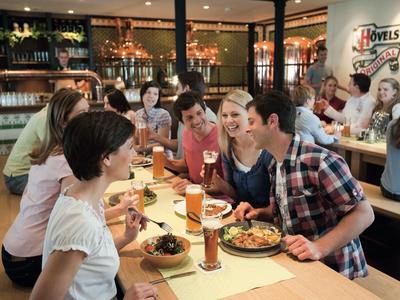 Grupa młodych osób siedzi przy nakrytym stole w restauracji, rozmawiając ze sobą.