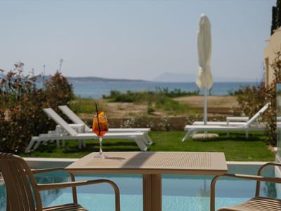 Blick von Terrasse mit Tisch und Stühlen auf Pool, Liegen, Meer und Insel im Hintergrund.