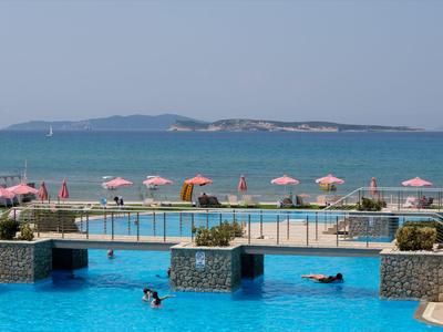 Großer Pool mit Schwimmern und rosa Sonnenschirmen am Meer mit Inseln im Hintergrund