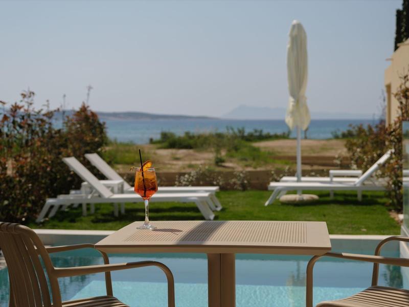 Blick von Terrasse mit Tisch und Stühlen auf Pool, Liegen, Meer und Insel im Hintergrund.