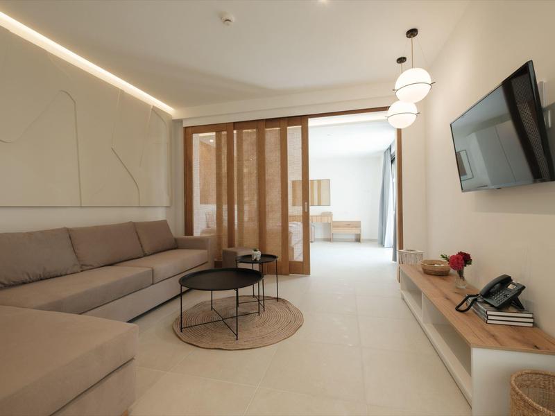 Moderner Wohnraum mit grauem Ecksofa, runden Tischen, Holzregal und Wand-TV, heller Boden und Deckenlampen.