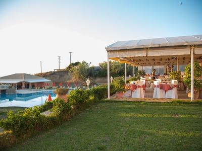 Restaurant en plein air à côté de la piscine avec vue sur l'hôtel et le jardin au coucher du soleil.