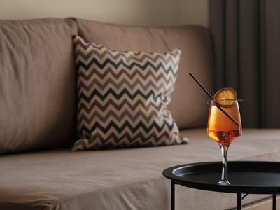 Cocktail con fetta d'arancia su tavolino nero davanti a divano beige con cuscino a zigzag.