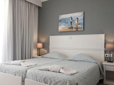 Camera d'hotel moderna con letto matrimoniale, parete grigia, tende e quadro della spiaggia sopra la testiera.