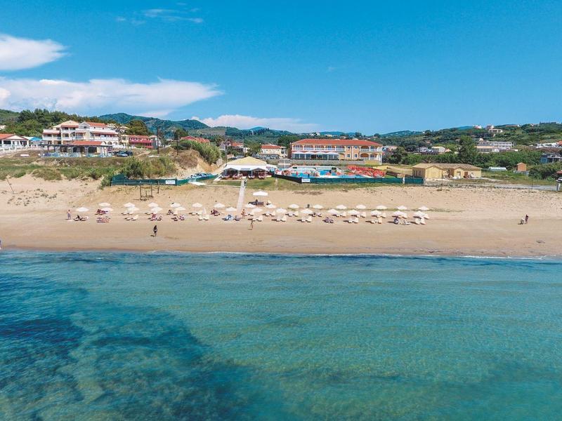 Spiaggia con ombrelloni e hotel sullo sfondo sotto un cielo blu.