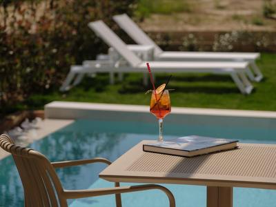 Ein Cocktail und ein Buch auf einem Tisch, im Hintergrund ein Pool und Sonnenliegen im Garten.