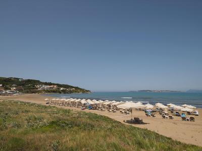 Strand mit Sand, weißen Sonnenschirmen, ruhigem Meer und klar blauem Himmel im Hintergrund.
