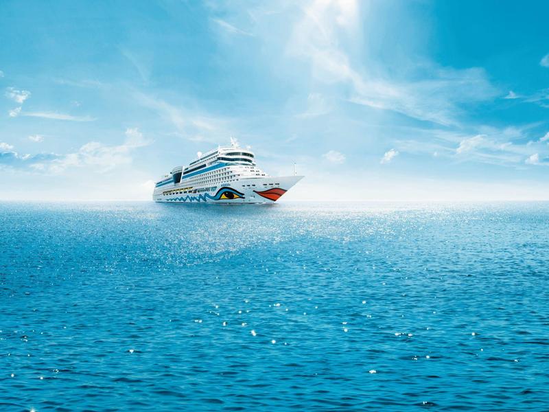 Großes weißes Kreuzfahrtschiff fährt auf ruhiger, blauer See unter hellem, bewölktem Himmel.