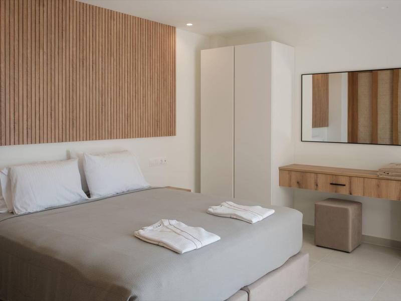 Schlafzimmer mit grauem Bett, weißen Handtüchern, kleinem Hocker, Spiegel und Garderobenschrank.