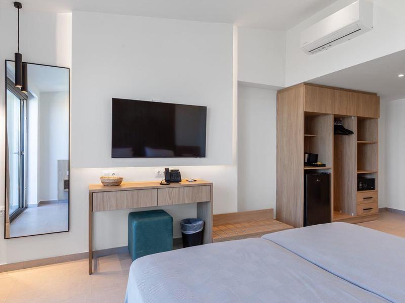 Modernes Schlafzimmer mit hellem Holz, grauer Bettdecke, großem Spiegel und Wand-TV.