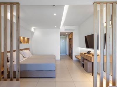 Moderner, heller Wohnraum mit grauem Bett, Holzelementen, Fernseher und fliesenboden.