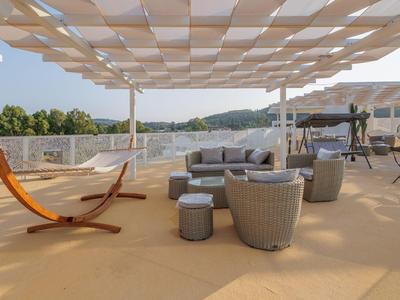 Terrazza sul tetto con lounge moderna, amaca e vista sulle colline verdi sotto un cielo azzurro.