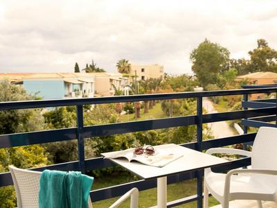 Balkon mit Stühlen und einem Tisch mit Zeitschrift und Getränken, Blick auf Bäume und Gebäude.