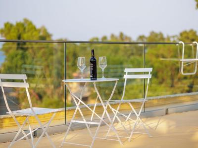 Small white garden table with two white chairs on terrace with glass railing and green view.