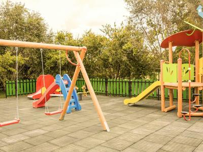 Ein Kinderspielplatz mit Schaukel, Rutsche und Klettergerüst auf einem gepflasterten Boden.