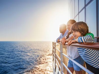 Des enfants s'appuient sur la rambarde d'un bateau en regardant la mer au coucher du soleil.
