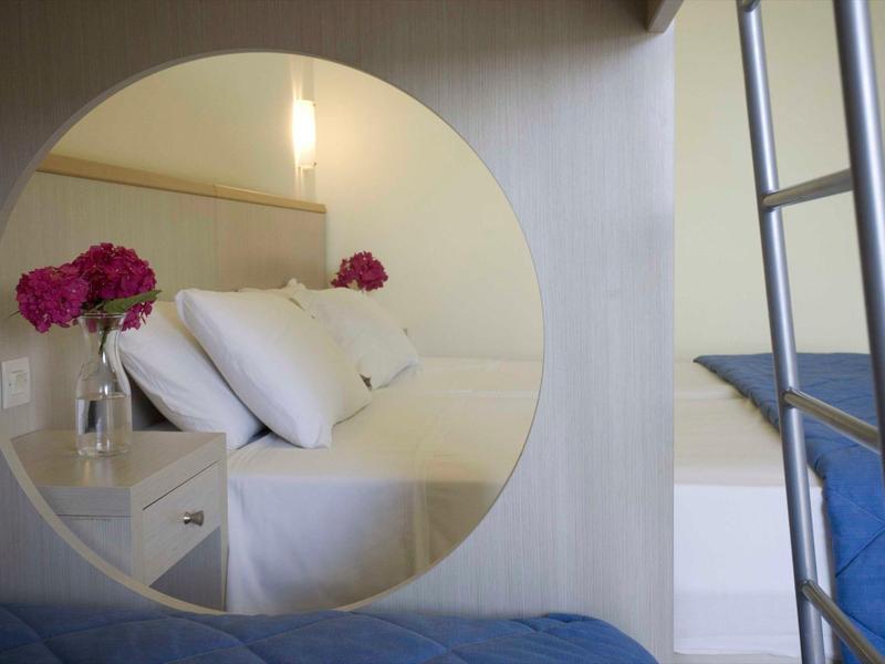 Spiegel reflektiert ein Bett mit weißen Kissen und rosa Blumen in Vase auf Nachttisch.