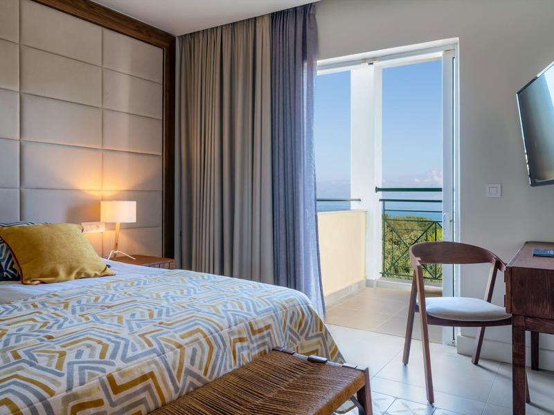 Gemütliches Schlafzimmer mit großem Bett, Holzmöbeln, Fernseher und Balkon mit Meerblick.