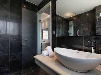 Modernes Badezimmer mit schwarzer Fliese, ovalem Waschbecken, großem Spiegel und heller Tür.