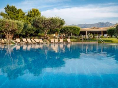 Grande piscine avec parasols et chaises longues dans un cadre de jardin verdoyant.