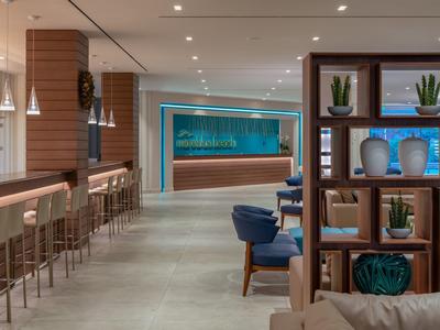 Moderner Gastraum mit Bar, blauen Sesseln, dekorativen Regalen und indirekter Beleuchtung.