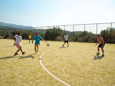 People playing soccer on a sunny outdoor field with mountain backdrop.