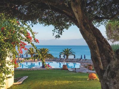 Vue à travers des arbres sur une piscine avec des palmiers et la mer en arrière-plan.
