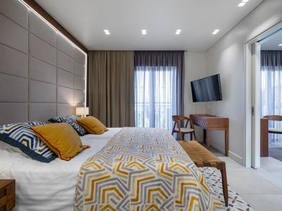 Modernes Schlafzimmer mit großem Bett, gemusterten Kissen, Holzmöbeln und indirekter Beleuchtung.